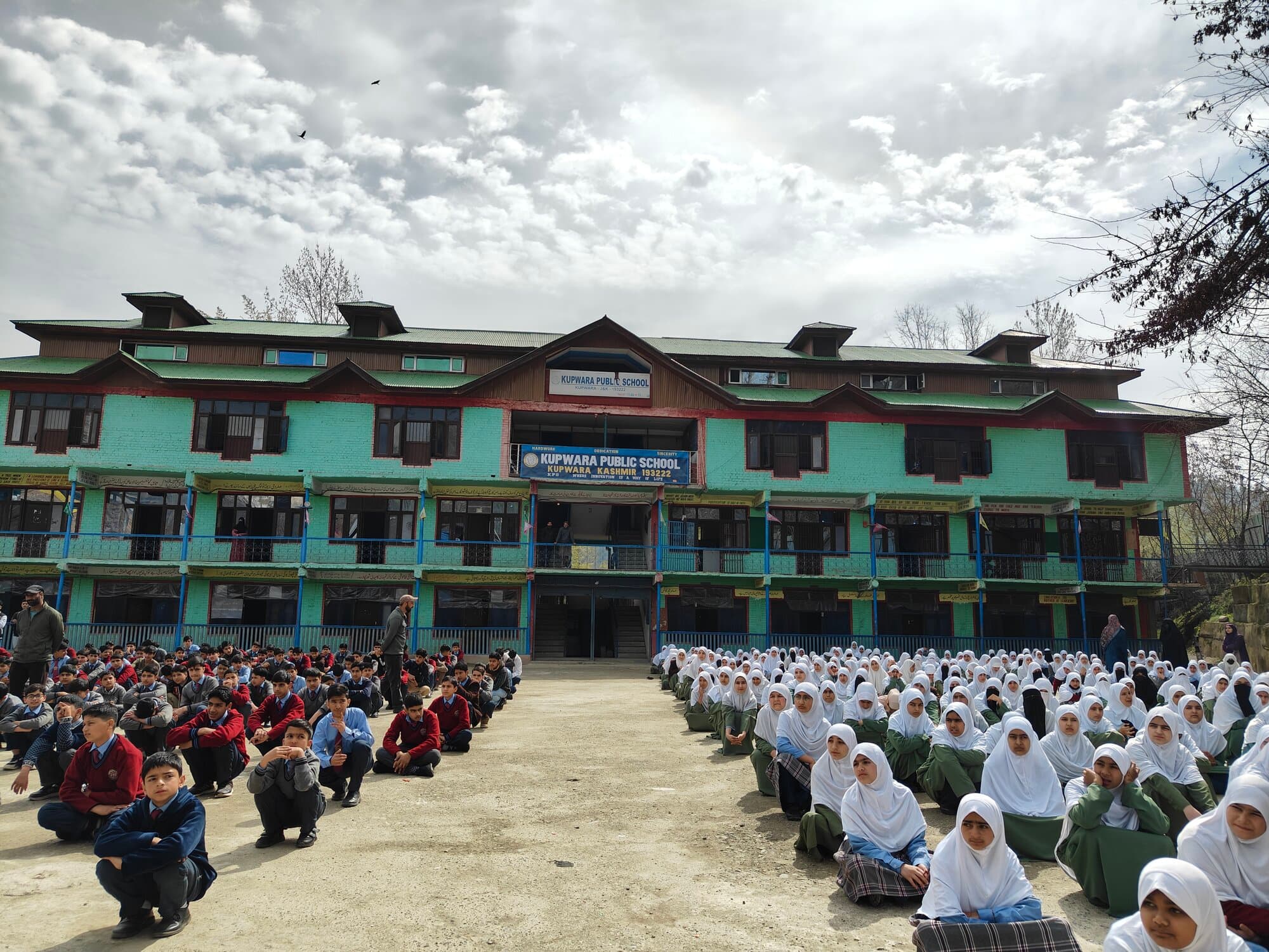 Students assembled in front of the school building under a cloudy sky